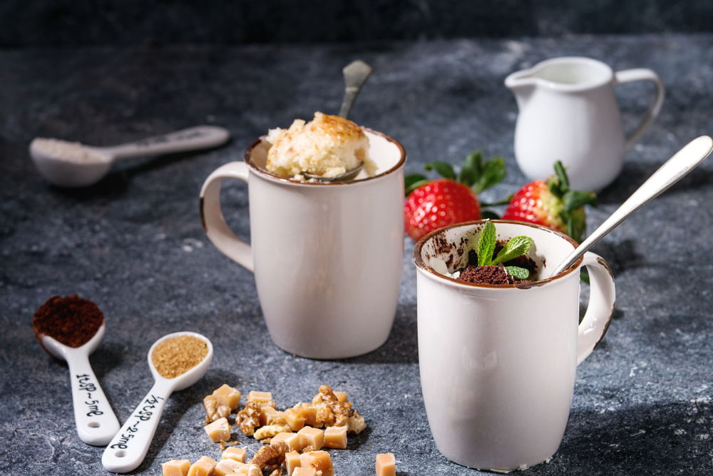 Čokoládový a vanilkový mugcake s jahodami v bielych hrnčekoch s lyžičkou